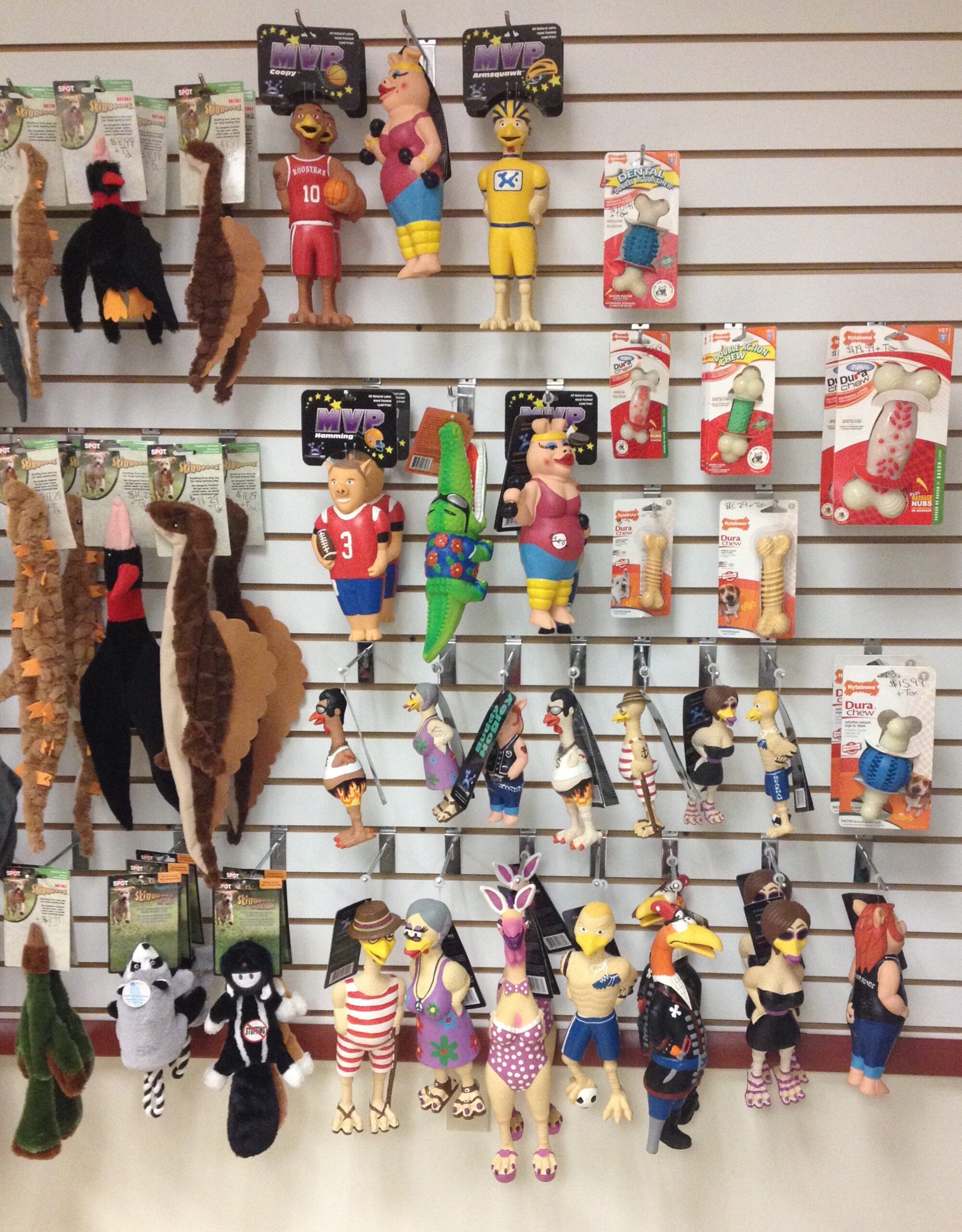 A variety of colorful, humorous dog toys displayed on a wall, featuring different characters such as athletes and animals, appealing to pet owners.