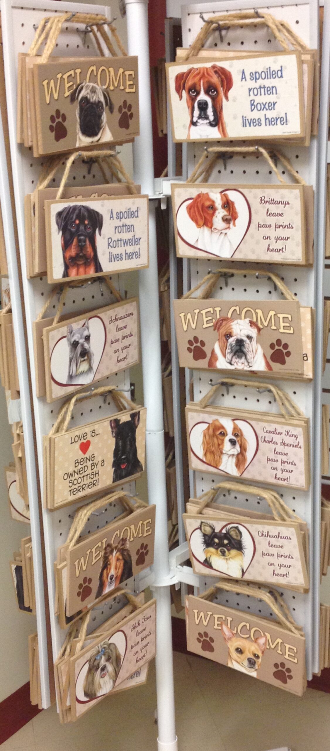 Colorful wooden signs featuring various dog breeds, highlighting playful phrases about pets, displayed on a rack in a store.
